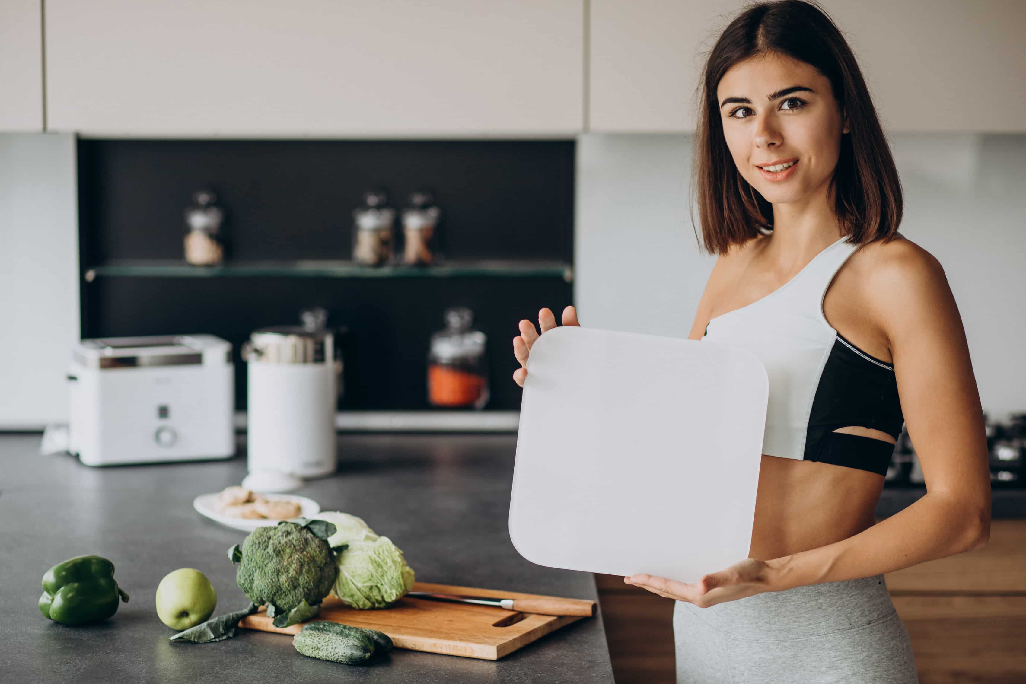 Best Nutrition Plans for Fitness 2 - mistalife Woman in a kitchen holds a white cutting board while fruits and vegetables sit on the counter, including broccoli and peppers.